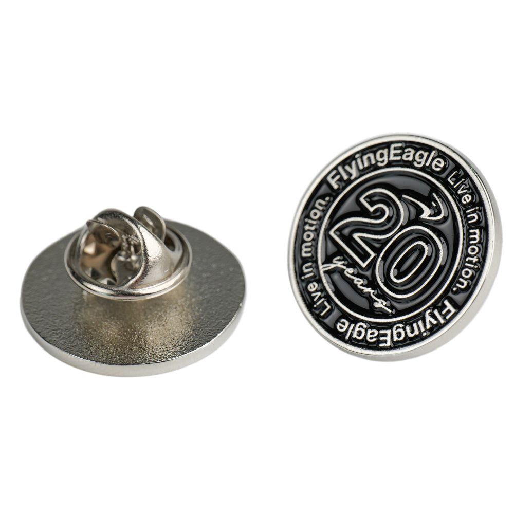 A round metal lapel pin shown from both sides on a white background. The front side features a silver and black design with the text 'FlyingEagle Live in motion.