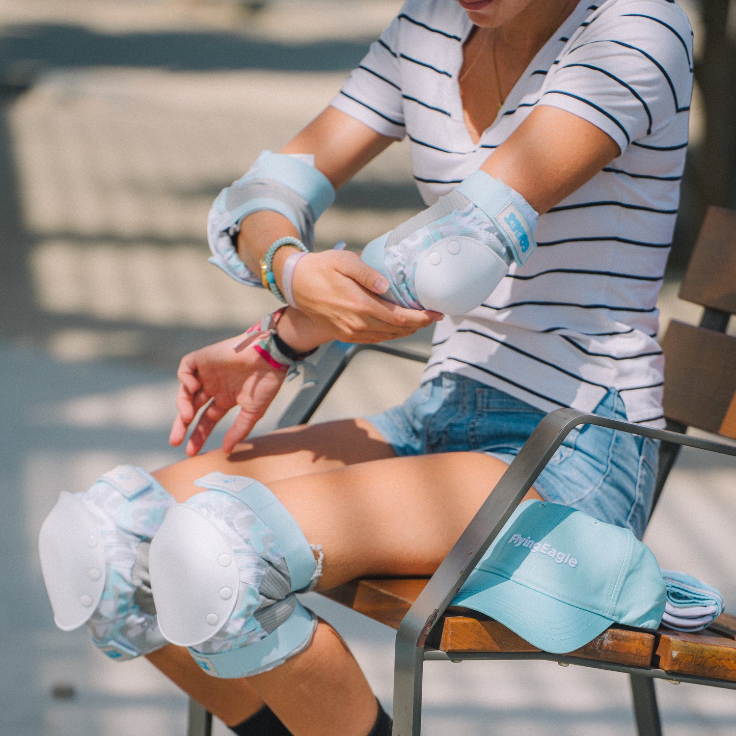 A woman sitting on a wooden bench outdoors wearing Flying Eagle COBET blue protective pads, including elbow pads, knee pads, and a matching cap.