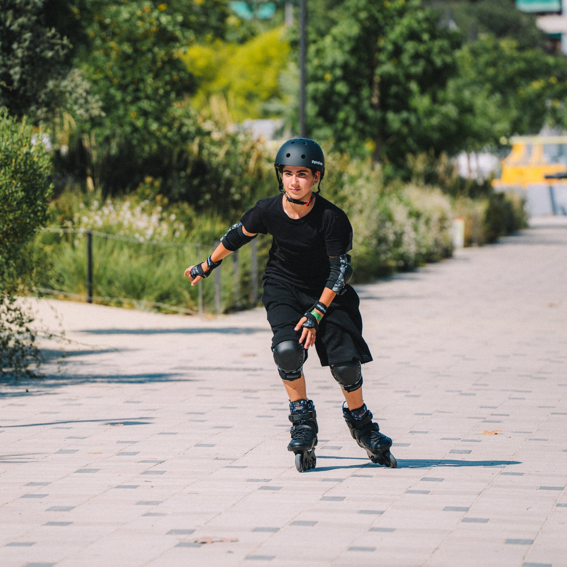 Skater gliding on flat pavement with Flying Eagle SHRIKE black 4-wheel hard boot inline skates for urban fitness, and wearing Flying Eagle URBAN black skate helmet
