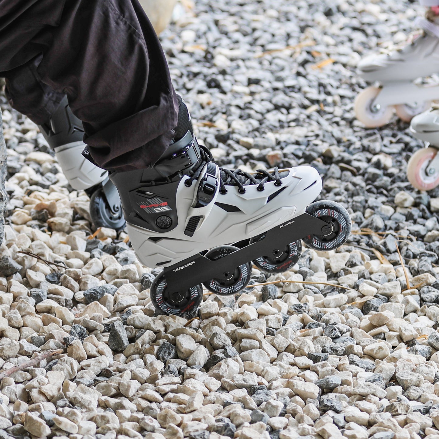 person seating with Flying Eagle SHRIKE SE asphalt grayinline skate  on a gravel path. 