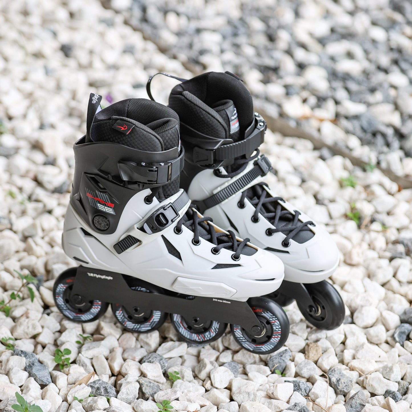 Flying Eagle SHRIKE SE asphalt gray inline skates with black wheels, placed on a bed of small white and gray gravel.