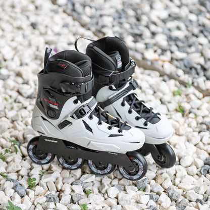 Flying Eagle SHRIKE SE asphalt gray inline skates with black wheels, placed on a bed of small white and gray gravel.