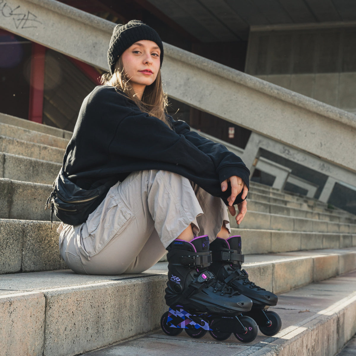 A woman sits on concrete outdoor stairs wearing FlyingEagle REAVER black‑violet fitness inline skate