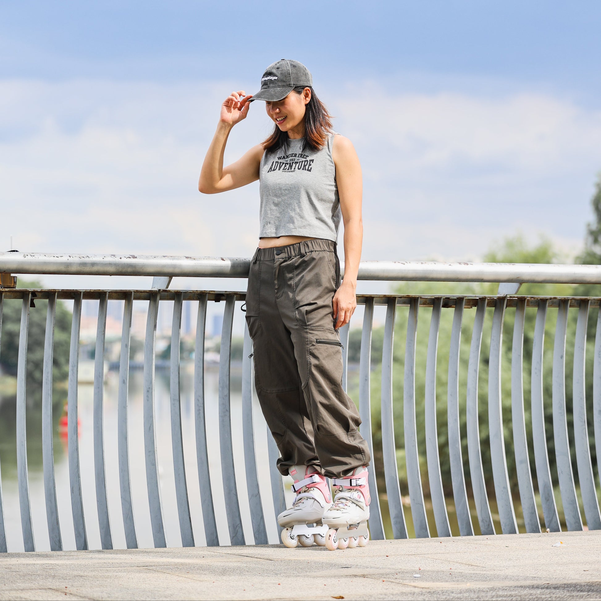 A woman wearing Flying Eagle SHRIKE SE peony pink 3‑wheel urban inline skate outdoors near a metal railing with a blue sky and water in the background.