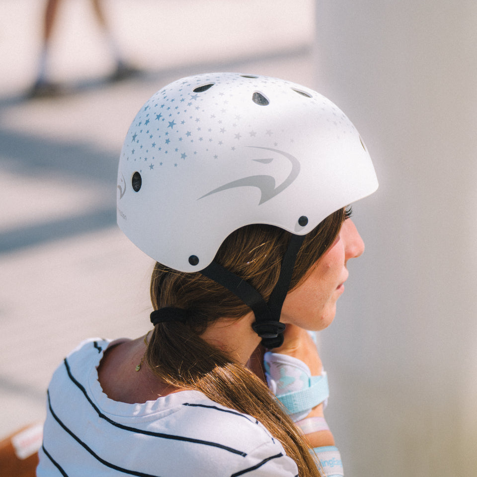 A woman in profile wearing Flying Eagle URBAN White Stars skate helmet  against a blurred outdoor background.